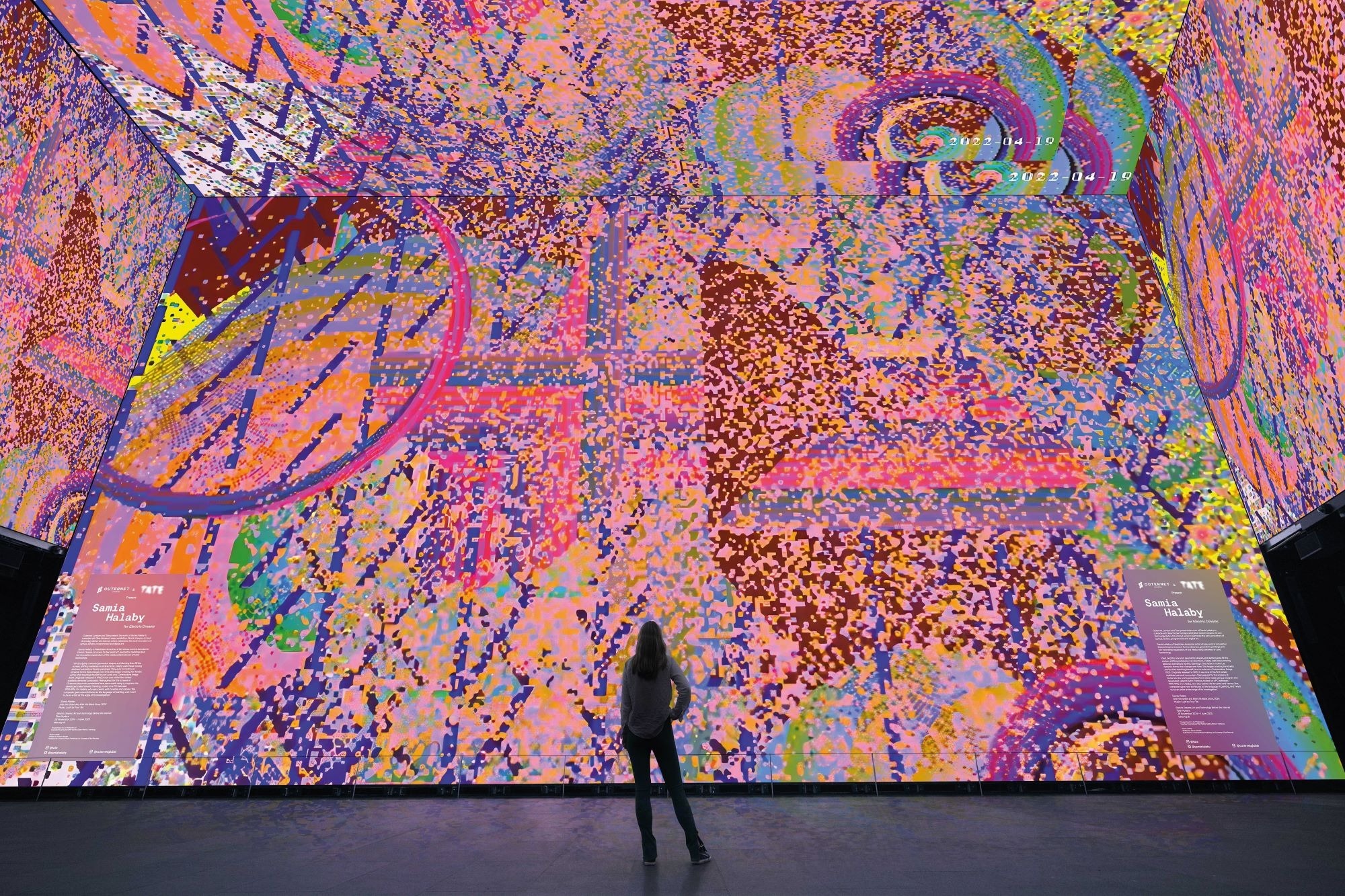 Outernet and the Tate present Samia Halaby for “Electric Dreams”. On display at Tottenham Court Road until 2 Feb. Photo courtesy of Tate and Outernet The walls of a room are covered in swirling pink designs as part of an art installation by Samia Halaby