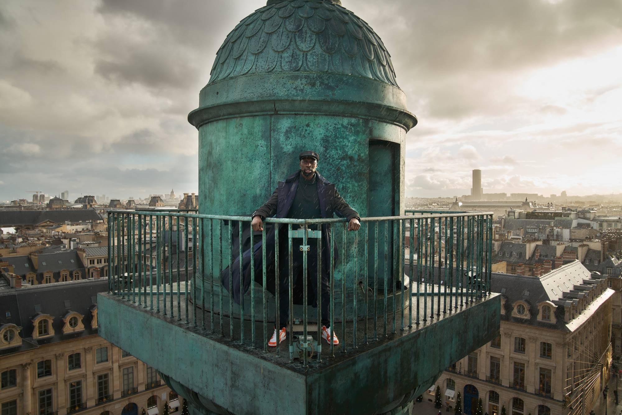 Omar Sy as Assane Diop in 'Lupin'. Credit: Emmanuel Guimier/Netflix Actor Omar Sy stands on top of a tower overlooking the Paris skyline in a scene from Lupin