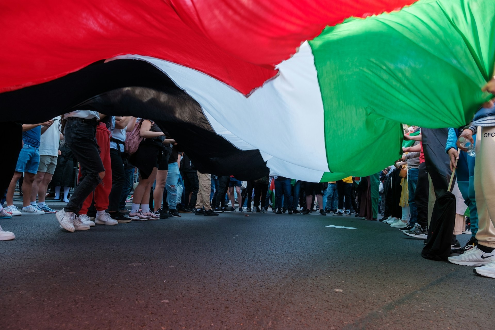 Protesters stand around a Palestinian flag in London. Credit: Ehimetalor Akhere Unuabona/Unsplash Protesters stand around a huge Palestinian flag during a protest in London