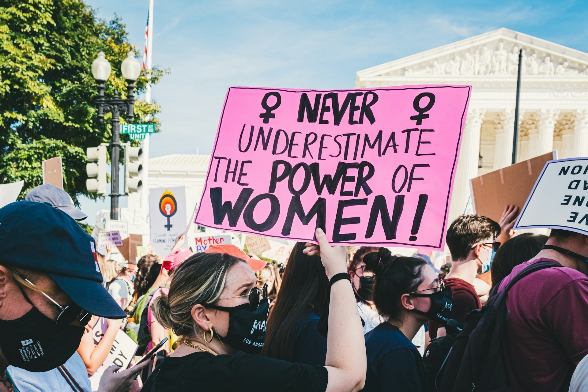 Women protest in Washington, DC. Credit: Gayatri Malhotra via Unsplash In the middle of a protest in Washington DC, a woman holds a sign reading 'Never underestimate the power of women'