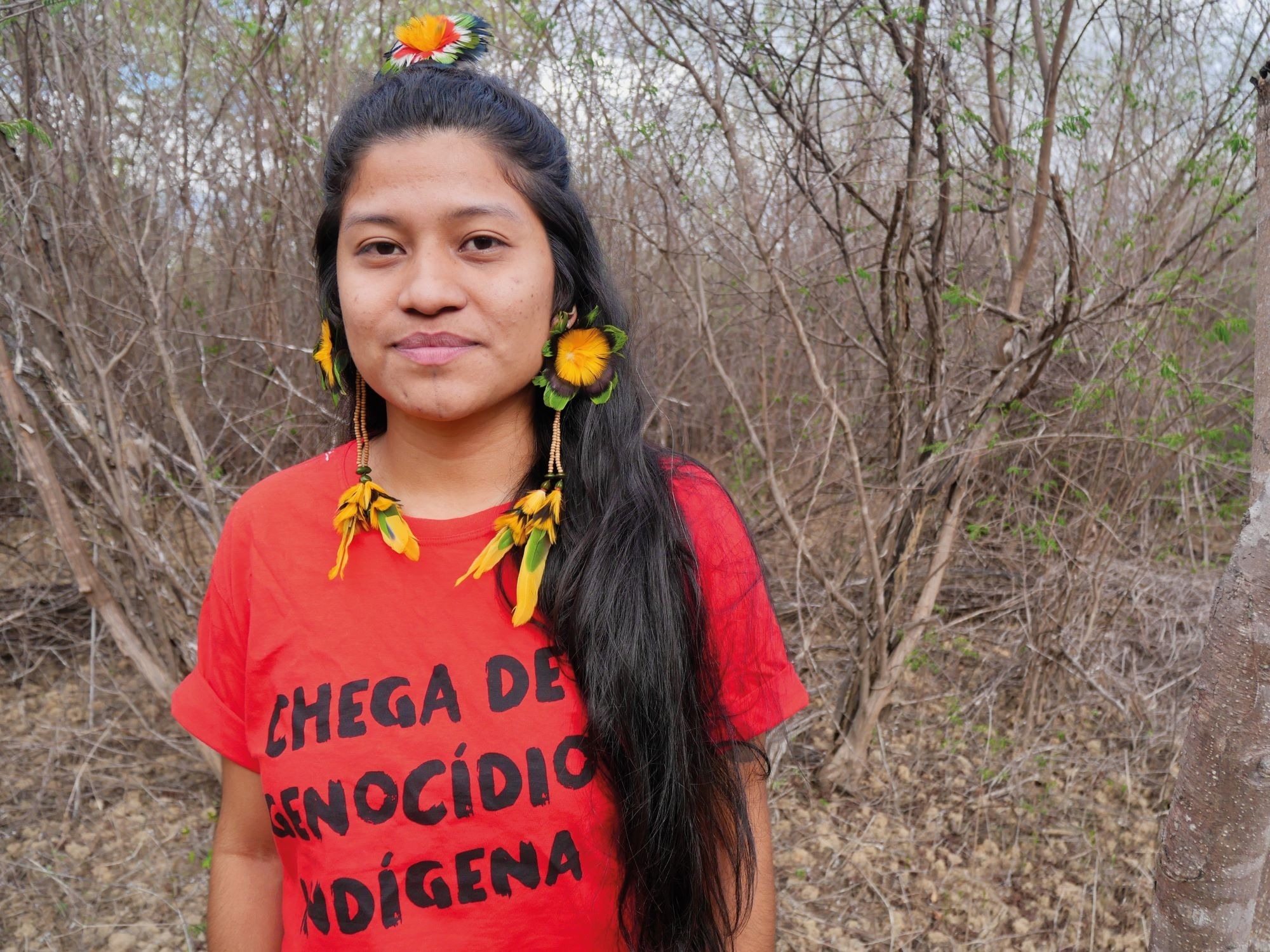 Ytxaha Pankararu Pataxó says her Indigenous village is surrounded by “megaprojects”. Credit: Eleonore Hughes Ytxaha Pankararu Pataxó wearing long feather earrings and a red T-shirt bearing the words “End the Indigenous genocide”